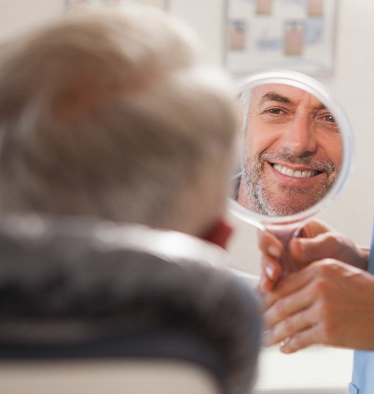 Man smiling at reflection in small, handheld mirror