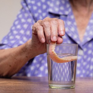 Hand placing dentures into glass of clear fluid