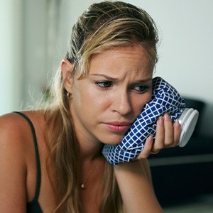 A woman holding an icepack to her jaw