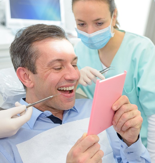 Man smiling at reflection with dentist looking over his shoulder