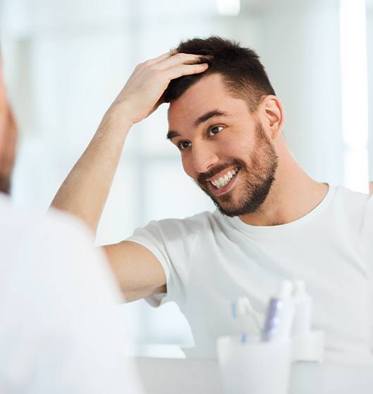 Patient in Rowlett smiling in mirror at dental implants