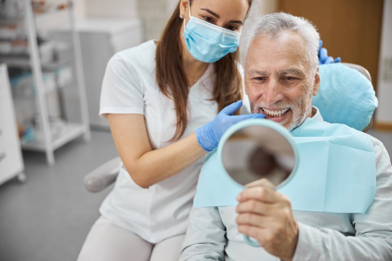 An older man admiring his new dental implant with a hand mirror