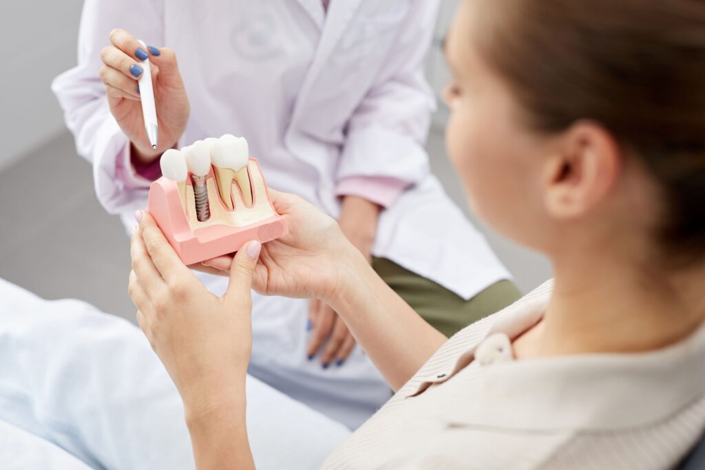 Patient holding model dental implant that dentist is gesturing to with pen