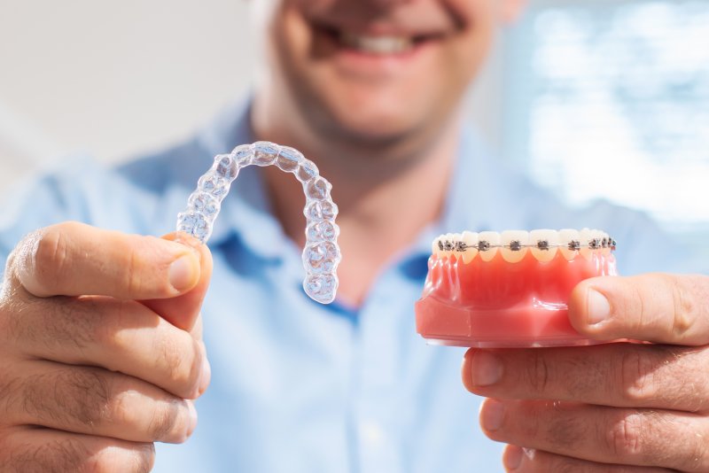 An orthodontist holding an aligner in one hand and a braces model in the other